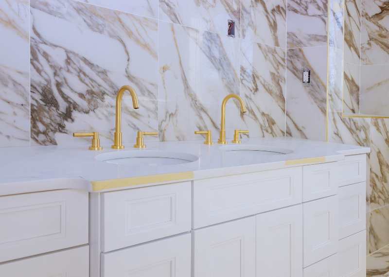 double sink gold faucet in gold and white bathroom
